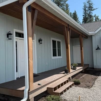 Modern house exterior with wooden porch, green siding, and landscaped entrance.