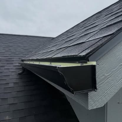 Gutter installation on a sloped roof with asphalt shingles, gray siding visible.