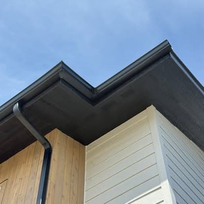 Modern building corner with black roof overhang and wooden siding under blue sky.