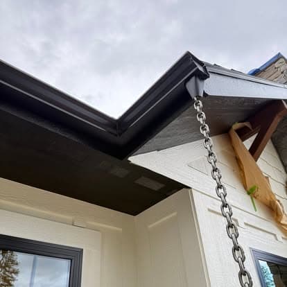Modern house eavestrough with black trim and chain, under cloudy sky.
