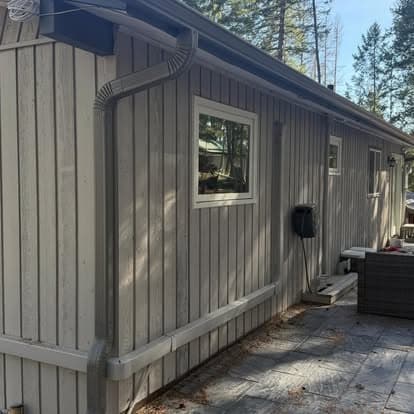 Wooden cabin exterior with gray siding, gutters, and windows in a forested setting.