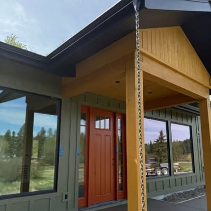 Modern house entrance featuring orange door, large windows, and wooden accents in a serene setting.