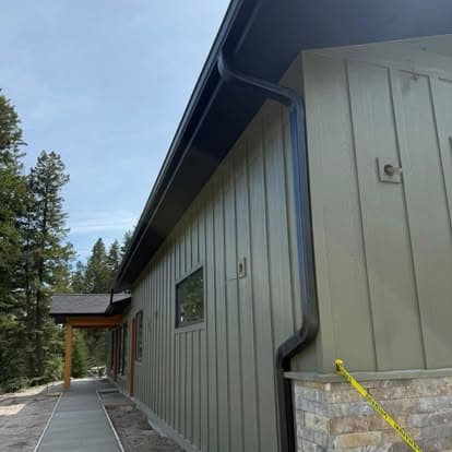 Modern green building exterior with stone accents and landscaping in a wooded area.