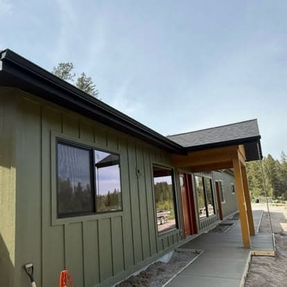 modern green house exterior with large windows and a wooden porch, surrounded by trees