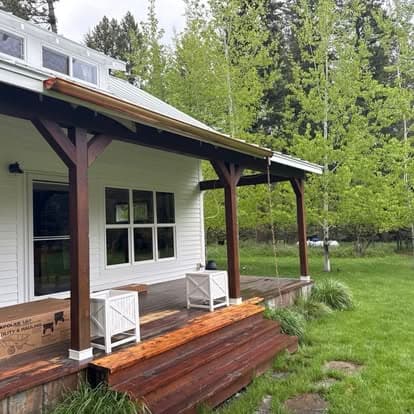 Charming porch with wooden steps, white chairs, and lush greenery in a serene outdoor setting.