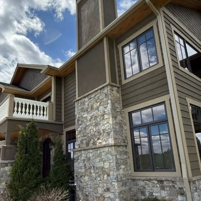 Modern stone and wood exterior of a luxury home under a blue sky with clouds.