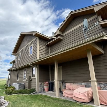 Modern two-story house exterior with brown siding, satellite dishes, and covered patio.