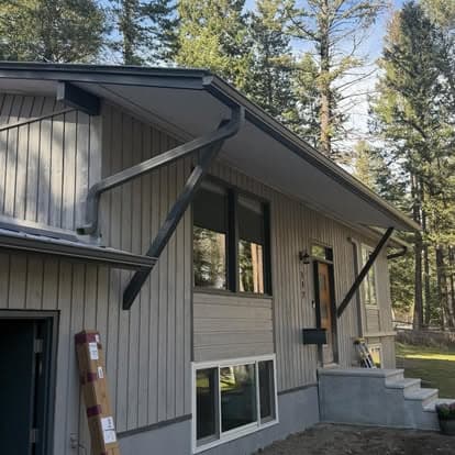 Modern home exterior with angular roof design, large windows, and surrounding trees.