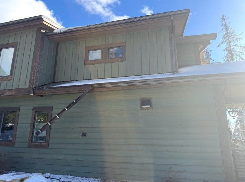 House exterior with green wood siding, winter scene, and snow on the roof.