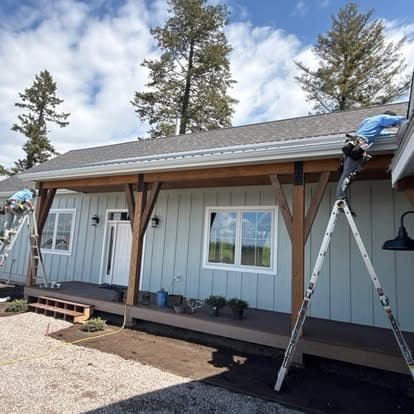 Exterior home renovation with workers on ladders, showcasing new roofing and wooden beams.