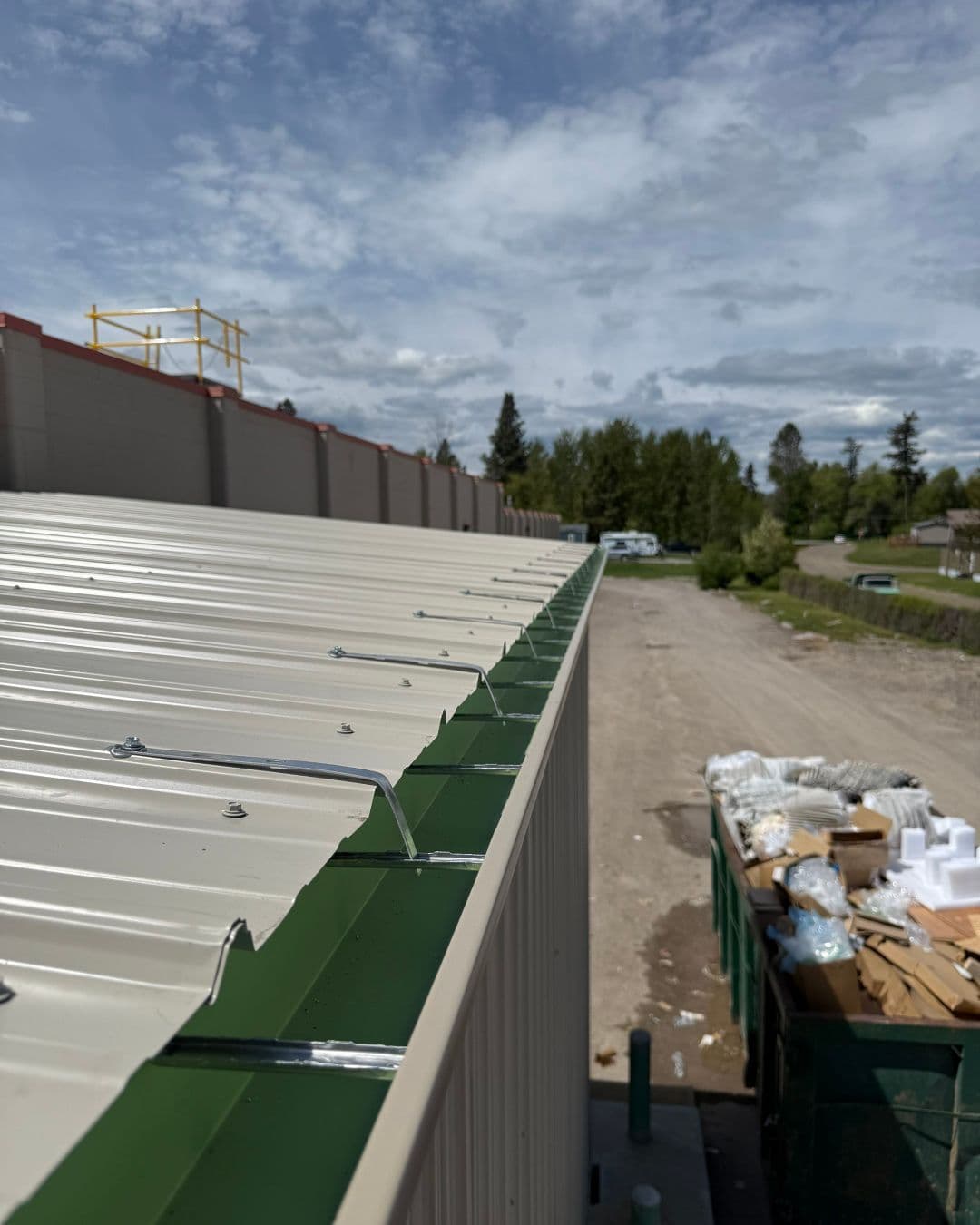 Roof edge of a building with green trim, construction site in the background under a cloudy sky.