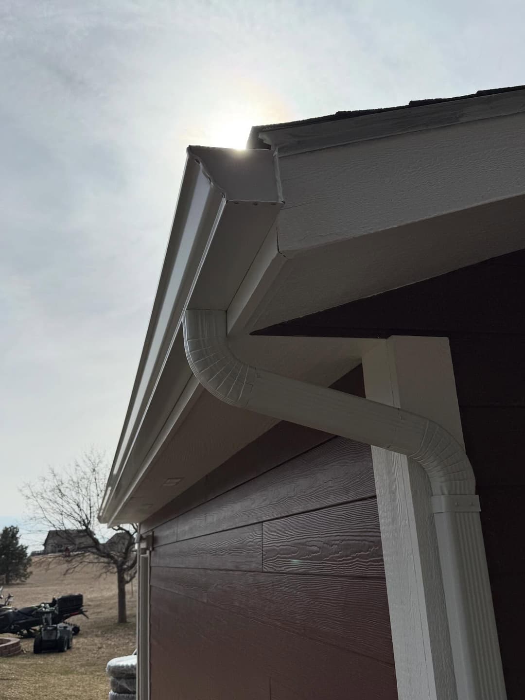 White gutter system on a house under a bright sky, emphasizing home drainage solutions.