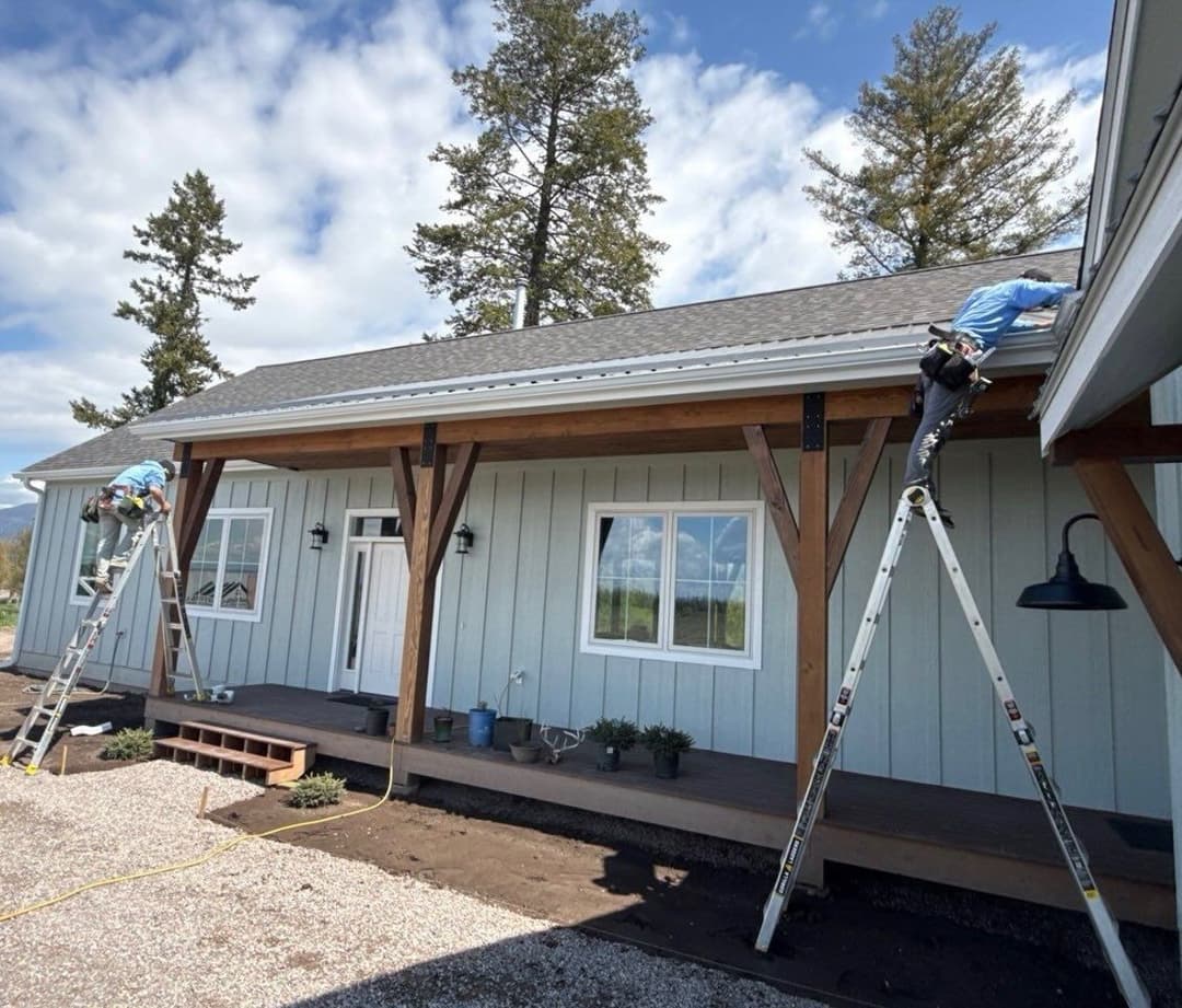 Workers installing a new roof on a blue house with wooden beams and a clear sky.