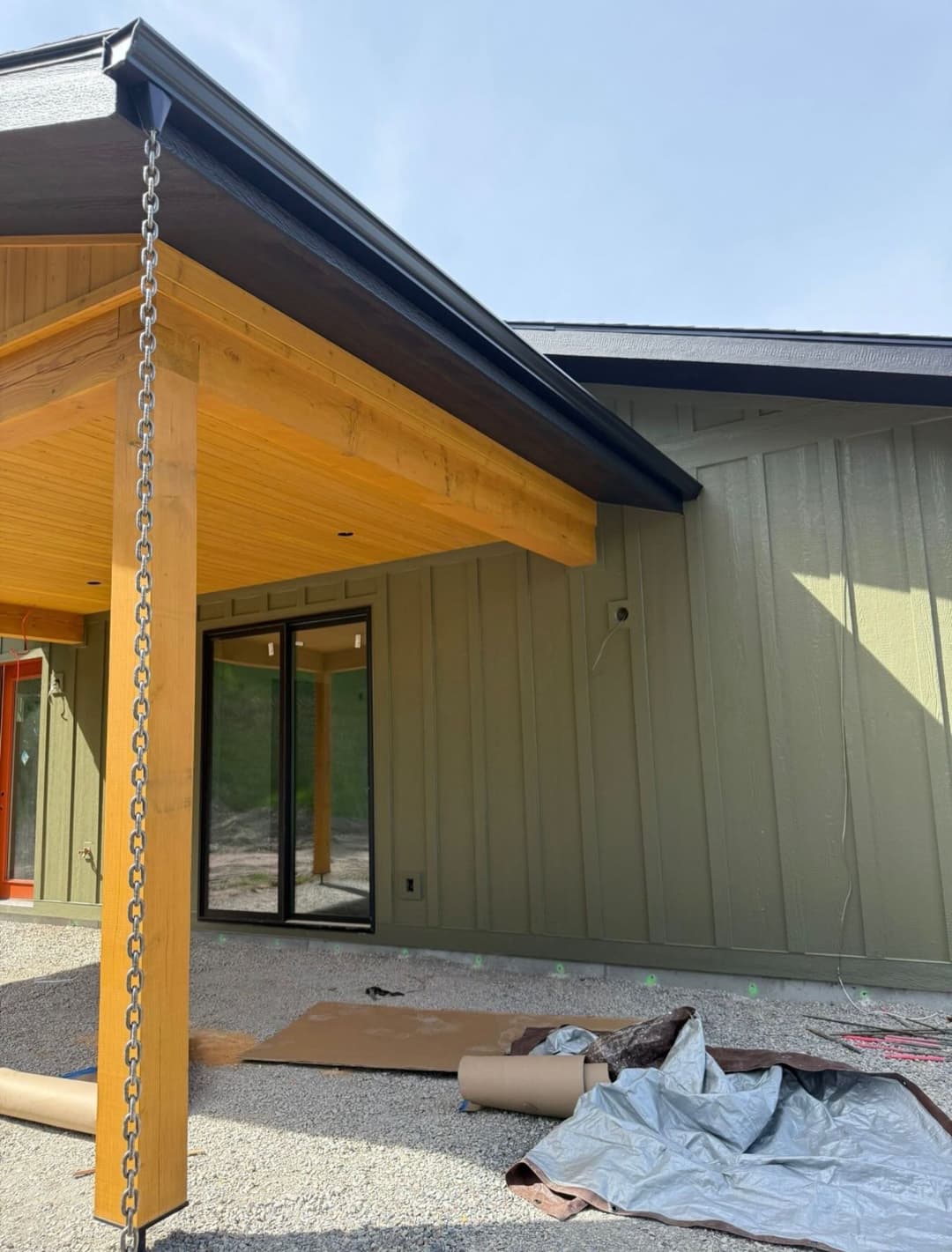 Modern house exterior featuring a wooden porch, metal roof, and construction materials on the ground.