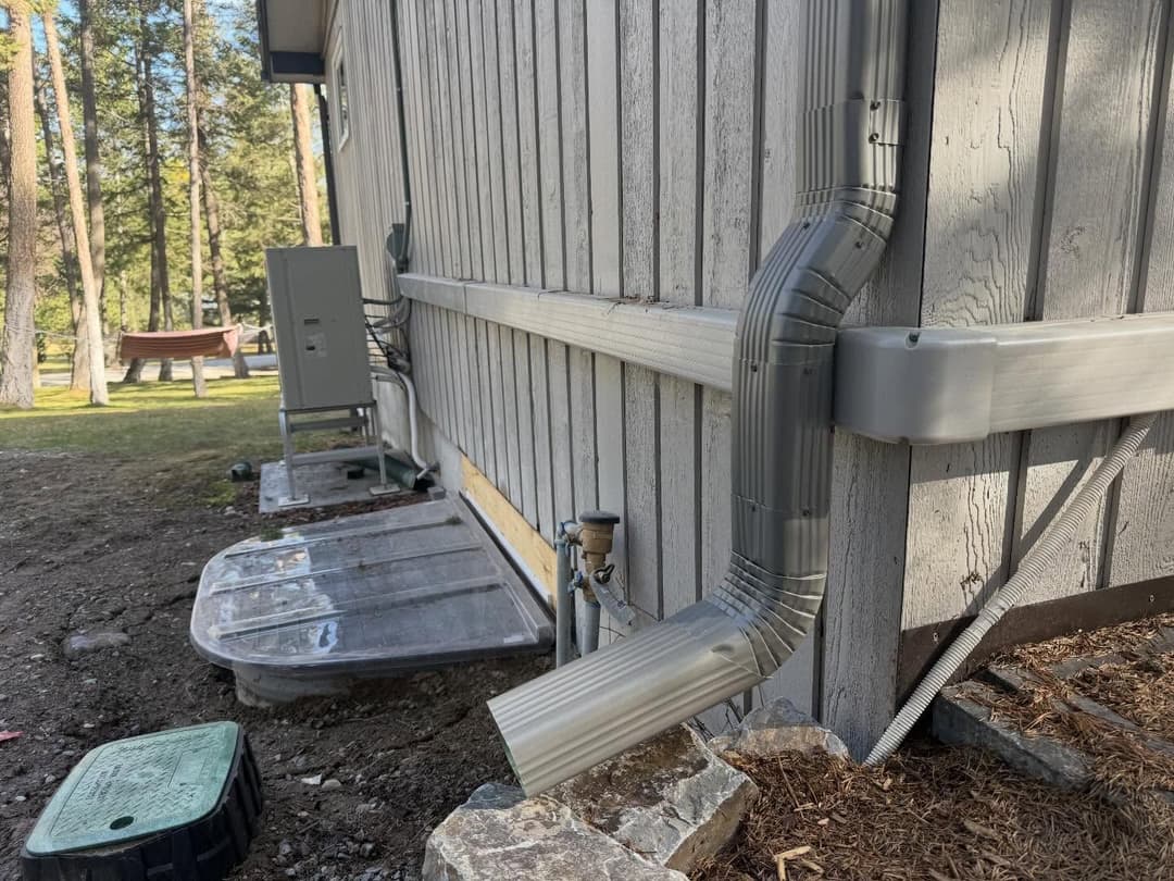 Rain gutter system directing water away from a wooden house in a forested area.