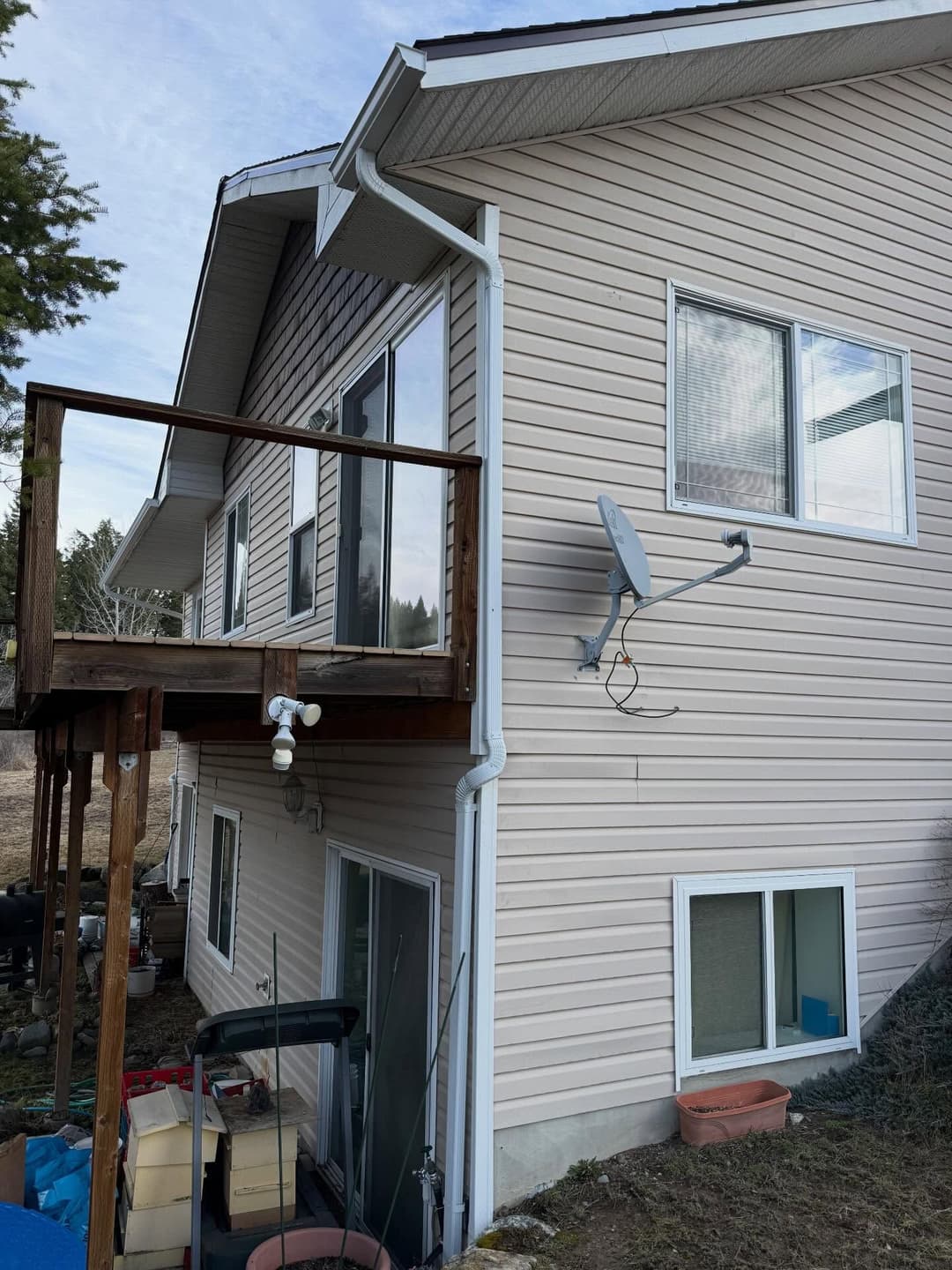 Two-story house exterior with deck, satellite dish, and outdoor storage.