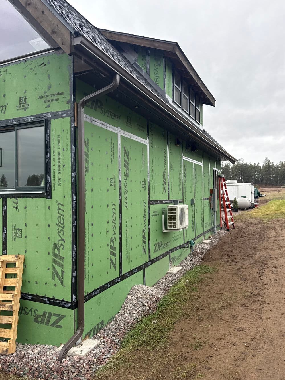 House under construction with green Zip System sheathing, ladder, and air conditioning unit.