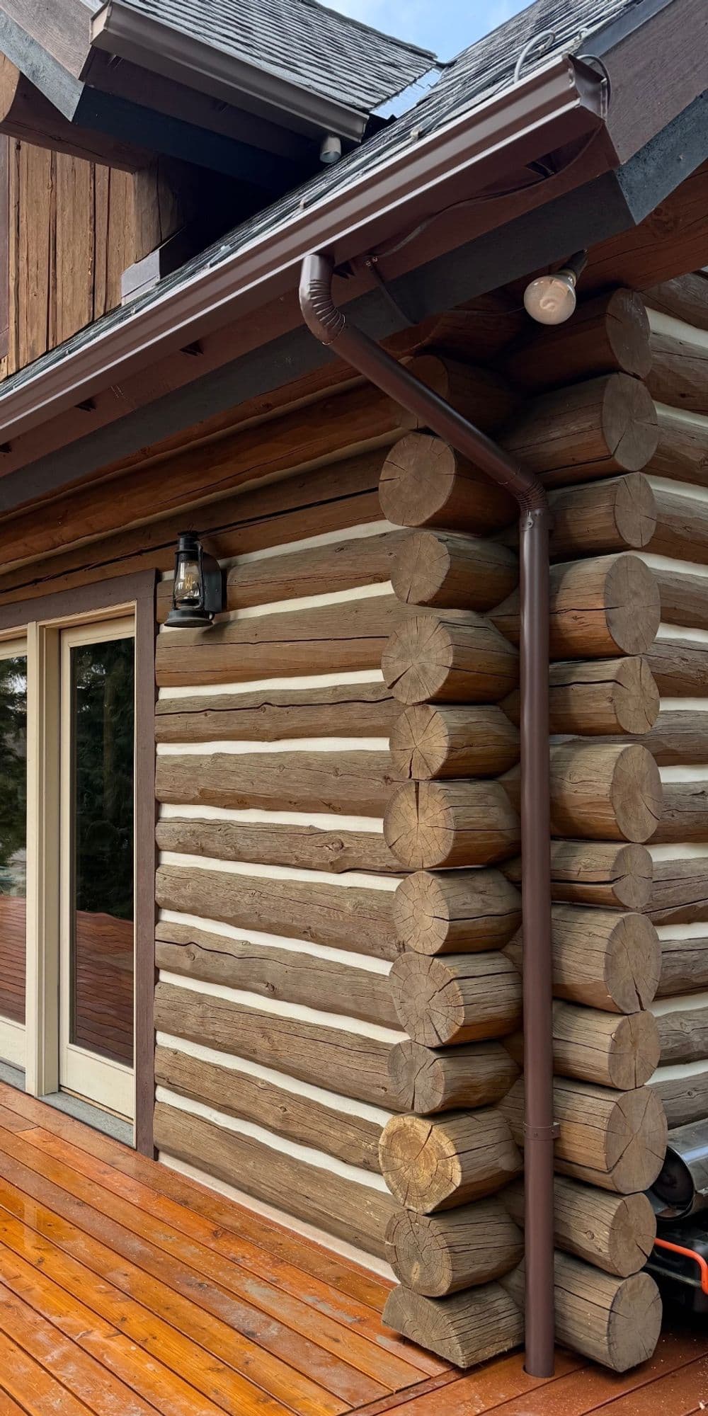 Log cabin corner with wooden siding and a brown downspout, showcasing rustic architecture.